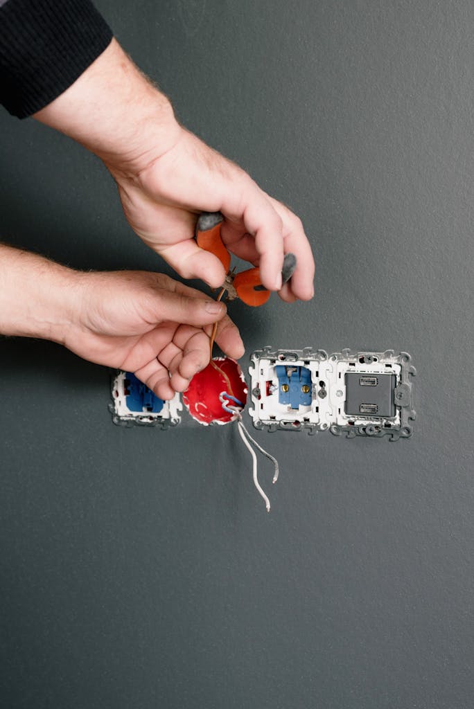 Crop anonymous electrician installing sockets and switches in room with gray walls in daytime